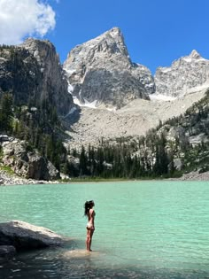 a woman standing in the water near mountains