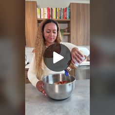 a woman mixing food in a bowl on top of a counter with a bookcase behind her