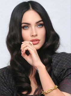 a woman with long black hair and blue eyes wearing a gold bracelet, posing for the camera