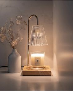 a table lamp sitting next to a vase with flowers in it and a lit candle