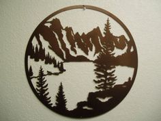 a metal circle with trees and mountains cut out of it's sides, hanging on a wall