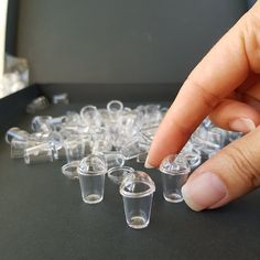 a hand reaching for small clear plastic cups on a table with one finger pointing at them