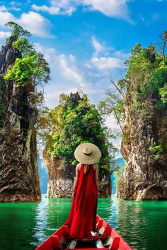 a woman in a red dress and straw hat is sitting on a boat looking out over the water