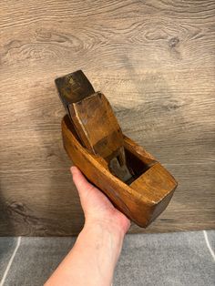 a hand holding a small wooden boat on top of a tile floor next to a wood paneled wall