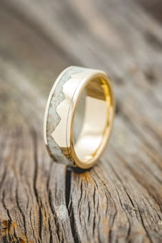 a gold wedding ring with white marble inlaying the center on a wooden surface