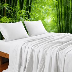 a bed with white sheets and pillows in front of bamboo trees