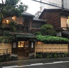 an old wooden building with green plants growing on it's roof line the street