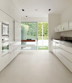 an empty kitchen with white cabinets and counter tops, along with glass doors leading to the outside