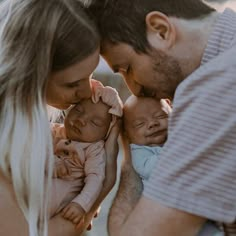 a man and woman holding two babys in their arms as they look at each other