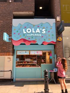 a woman standing in front of a cupcake shop next to a pole with a sign that says lola's curacies