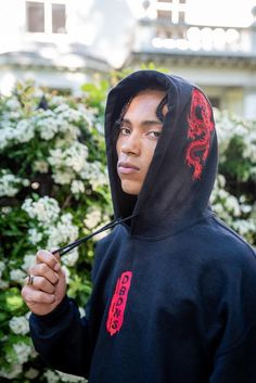 a young man with dreadlocks standing in front of trees Streetwear Hoodie With Embroidered Logo, Black Embroidered Hooded Hoodie, Hoodie Sweatshirt With Embroidered Logo For Streetwear, Urban Hoodie With Embroidered Logo For Streetwear, Streetwear Embroidered Fleece Sweatshirt, Red Sweatshirt With Embroidered Graphics For Streetwear, Red Embroidered Sweatshirt For Streetwear, Embroidered Long Sleeve Hoodie For Streetwear, Sporty Embroidered Hoodie For Streetwear