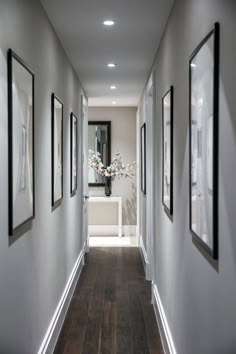 a long hallway with pictures on the wall and framed photos hanging on the walls, along with vases filled with flowers