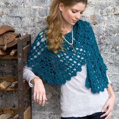 a woman standing next to a brick wall wearing a blue crocheted shawl