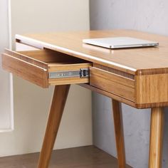 a laptop computer sitting on top of a wooden desk next to a white wall and floor