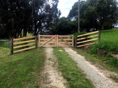 a wooden gate on the side of a dirt road next to a lush green field