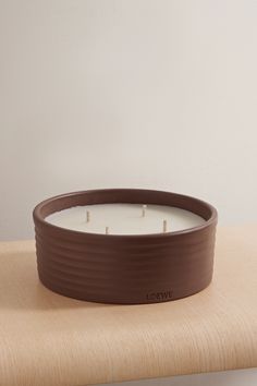 a brown candle sitting on top of a wooden table next to a white wall in the background