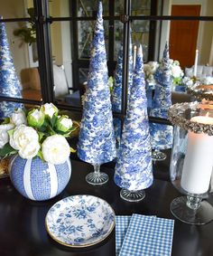 blue and white christmas decorations on a dining room table with candles, plates and flowers