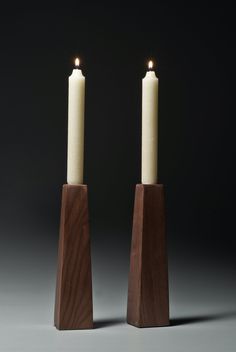 two wooden candlesticks with one lit and the other turned off in white light