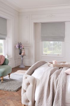 a bedroom with white walls and wooden flooring, two windows covered in roman shades