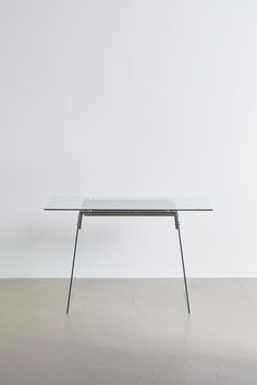 a glass table sitting on top of a cement floor next to a white wall in an empty room