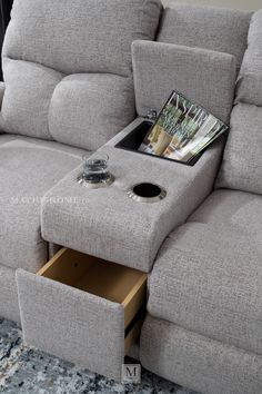 a grey couch with a magazine on it and a cup holder underneath the arm rest