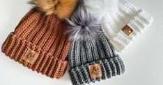 three knit beanies with pom - poms are lined up on a white surface