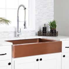 a copper sink in a white kitchen next to a window with potted plants on it