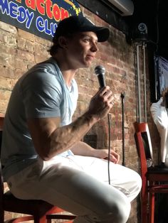 a man sitting in front of a microphone on top of a wooden chair next to a brick wall