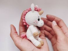 a hand holding a tiny crocheted white and pink unicorn