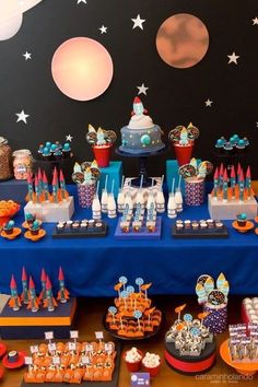 a blue table topped with lots of cupcakes and cake covered in frosting