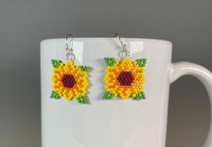 a pair of sunflower earrings made out of seed beads on a mug cup,