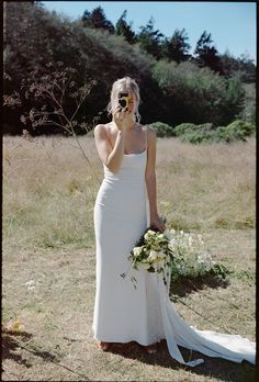 a woman in a white dress is holding a bouquet and talking on her cell phone