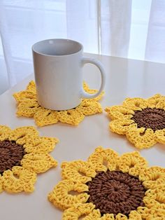 four crocheted sunflower coasters sitting on a table next to a coffee cup