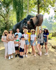 a group of people standing next to an elephant on a dirt ground with trees in the background