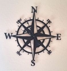 a metal compass mounted to the side of a white wall with black lettering on it