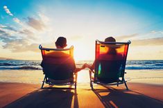 two people sitting in beach chairs facing each other on the beach with the sun setting behind them