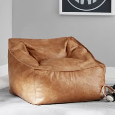 a brown leather bean bag chair sitting on top of a white floor next to a pair of black shoes