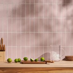 limes and wooden cutting board on counter in front of pink tiled backsplash