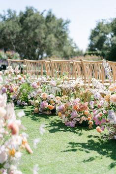 rows of wooden chairs lined up with flowers on the grass and in between them is an aisle