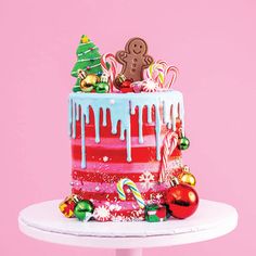 a christmas cake with icing and decorations on a white pedestal in front of a pink background