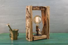 an old fashioned light bulb sits in a wooden frame next to a small metal cup