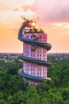 a tall pink building with a dragon on top in the middle of trees at sunset