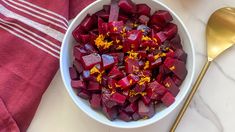 a white bowl filled with beets on top of a table next to a spoon