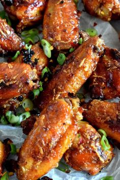 the chicken wings are covered in sauce and garnished with scallions on wax paper