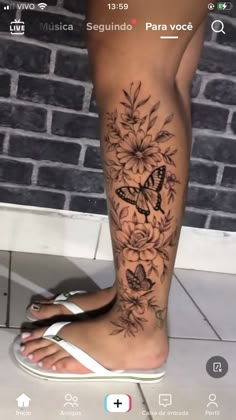 a woman's leg with flowers and butterflies on it, in front of a brick wall