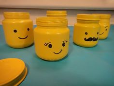 four yellow jars with faces drawn on them sitting on a blue counter top next to plates and bowls