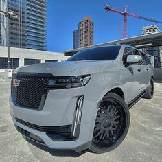 the front end of a silver suv parked in a parking lot next to tall buildings