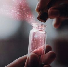 someone is holding a jar filled with pink liquid and sparkles in the air on their fingers