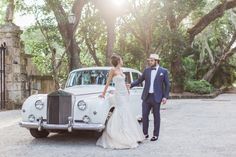 a bride and groom standing next to an old car