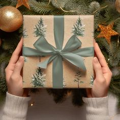 two hands holding a wrapped present in front of a christmas tree